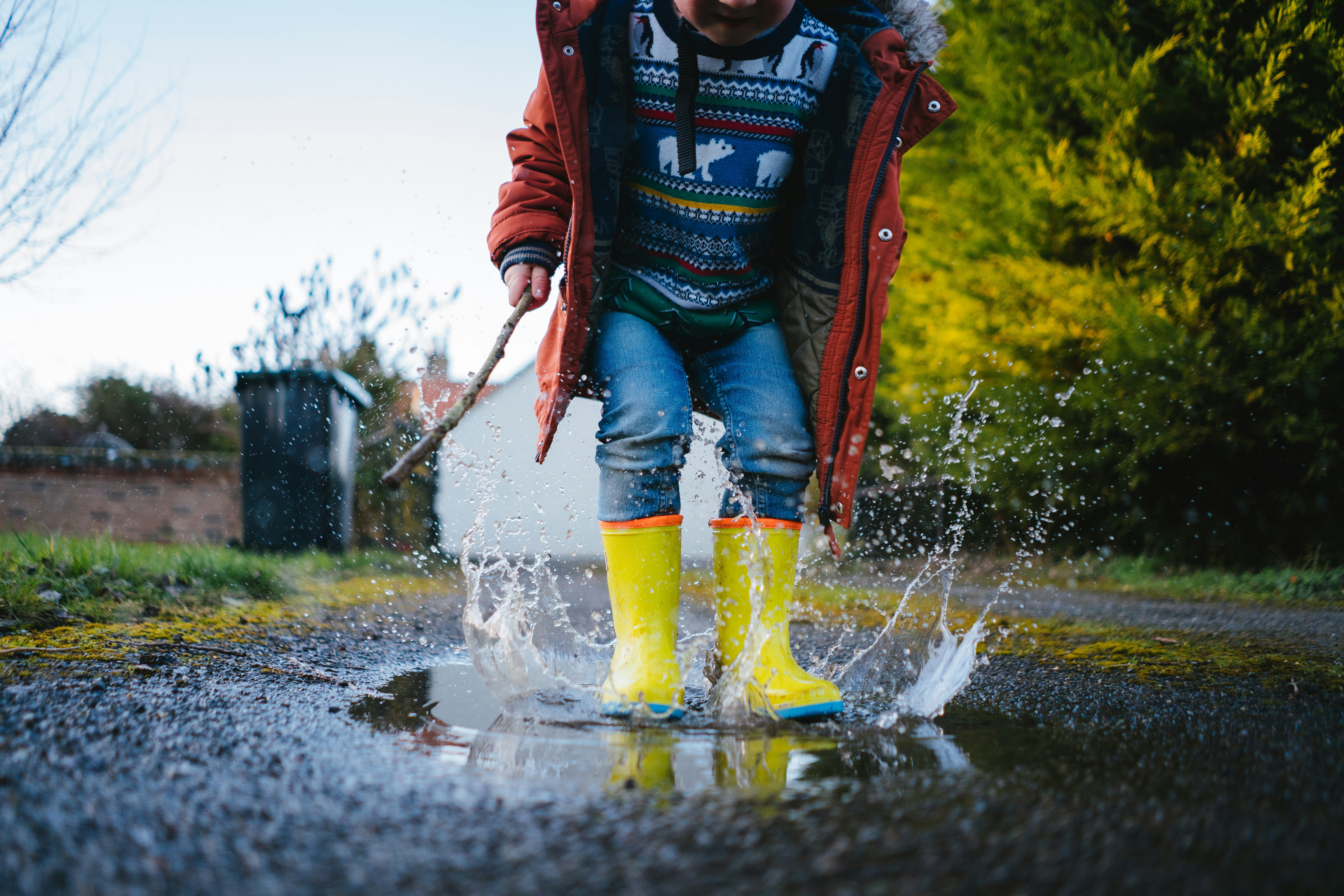 Kind mit gelben Gummistiefeln springt in eine Pfütze