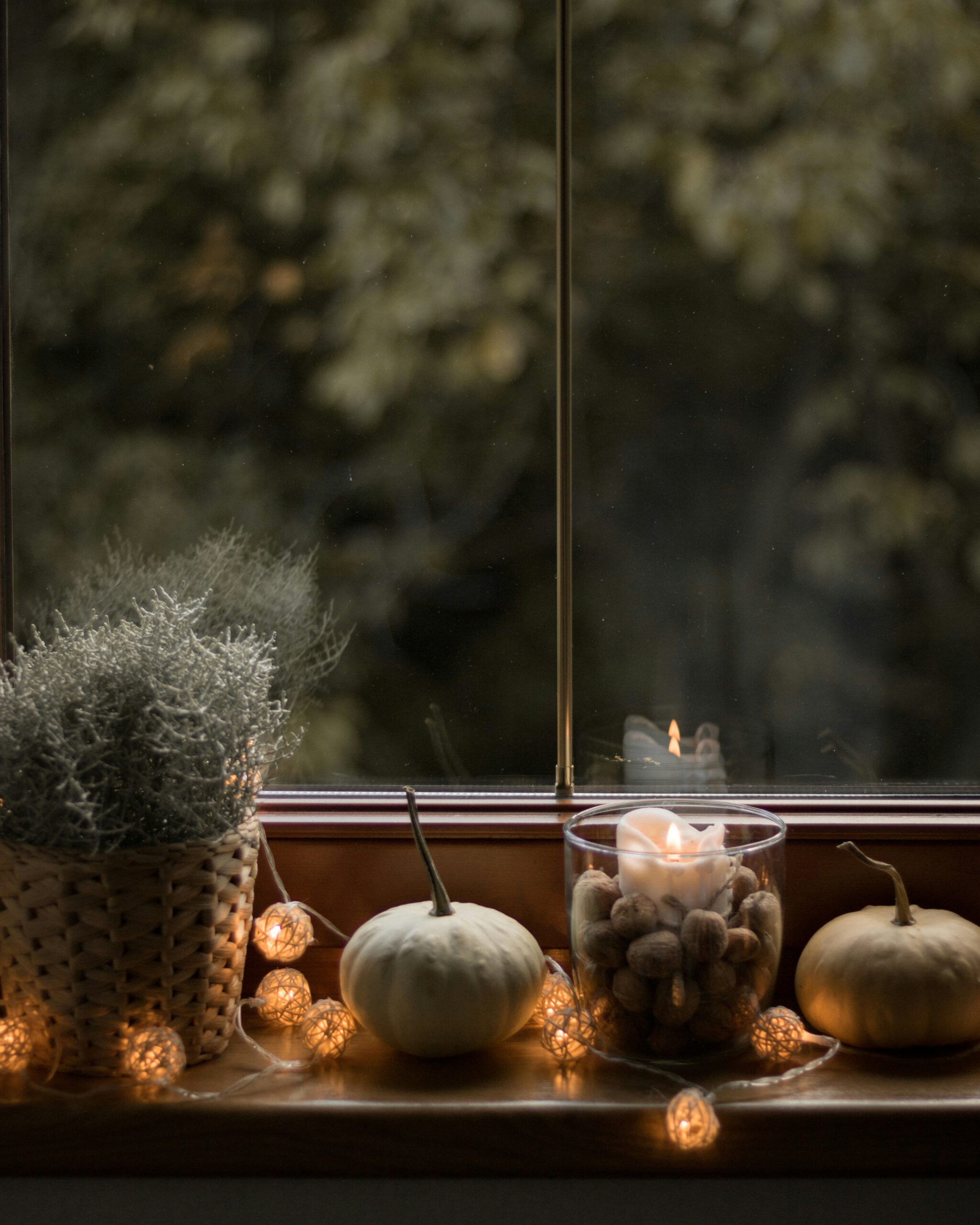 Kerze und kleine Kürbisse auf einer Fensterbank an einem dunklen Herbstabend
