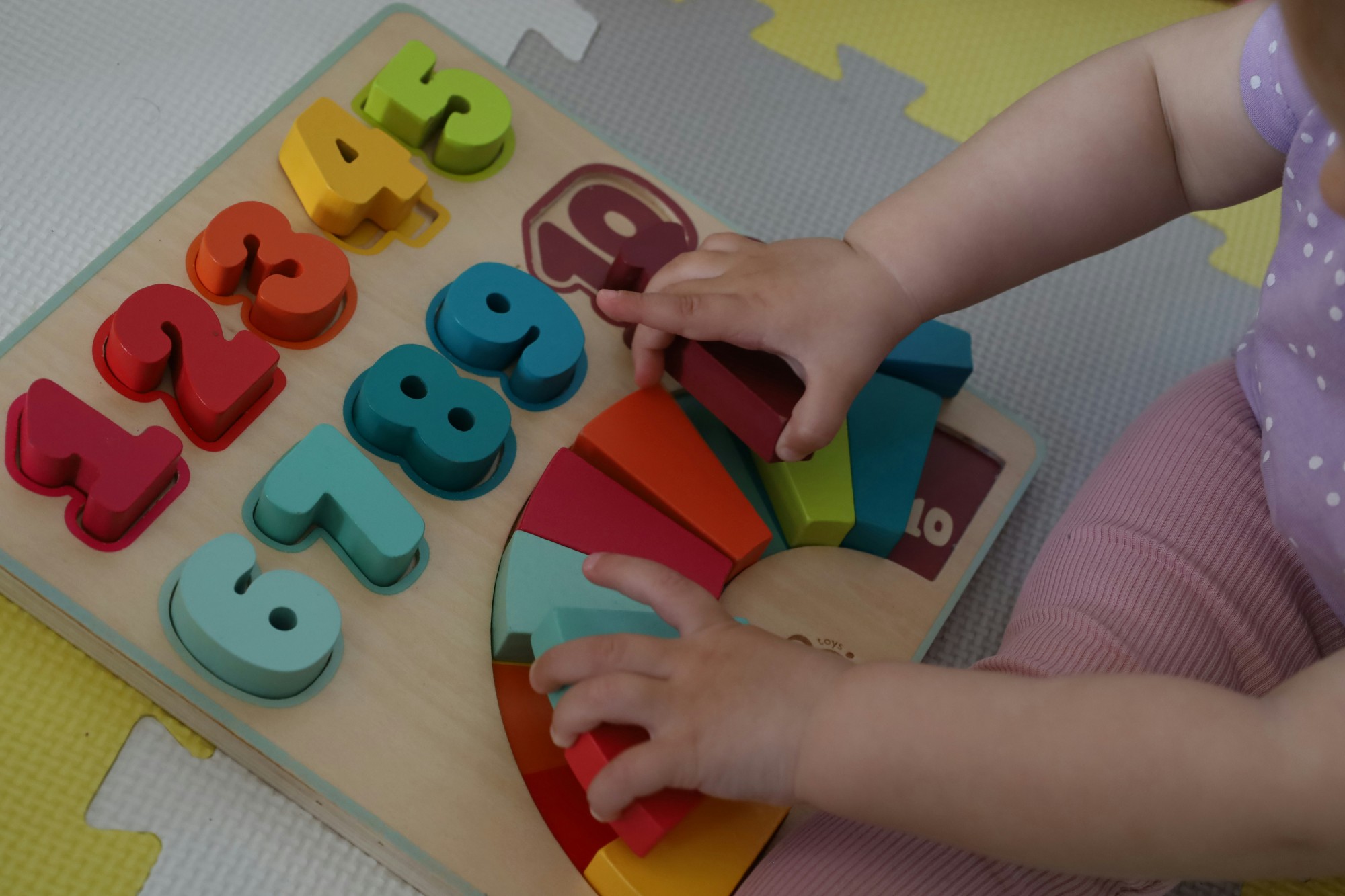 Kinderhände sortieren bunte Holzteile in ein Zahlenpuzzle
